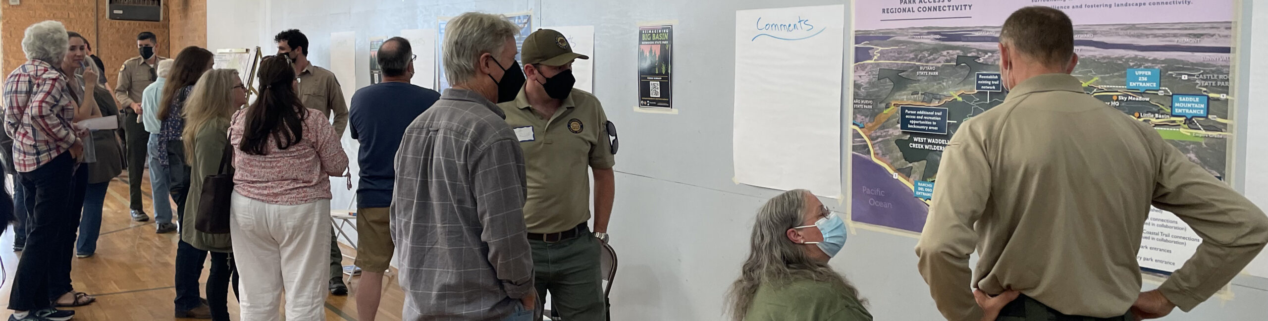 Several members of the public and park staff look at large maps pinned to the wall at a meeting to discuss future park plans.